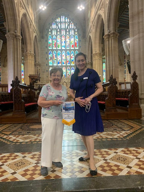 At St. Andrews Cathedral, Ann Webb presents our flag to Phoebe Alexander of Sydney Rotary Club.